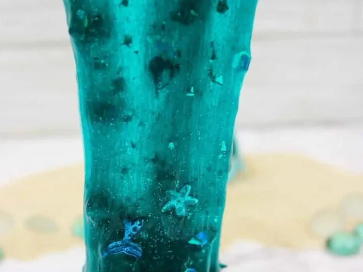 Shimmery teal mermaid slime with glitter and star confetti being stretched over a white surface