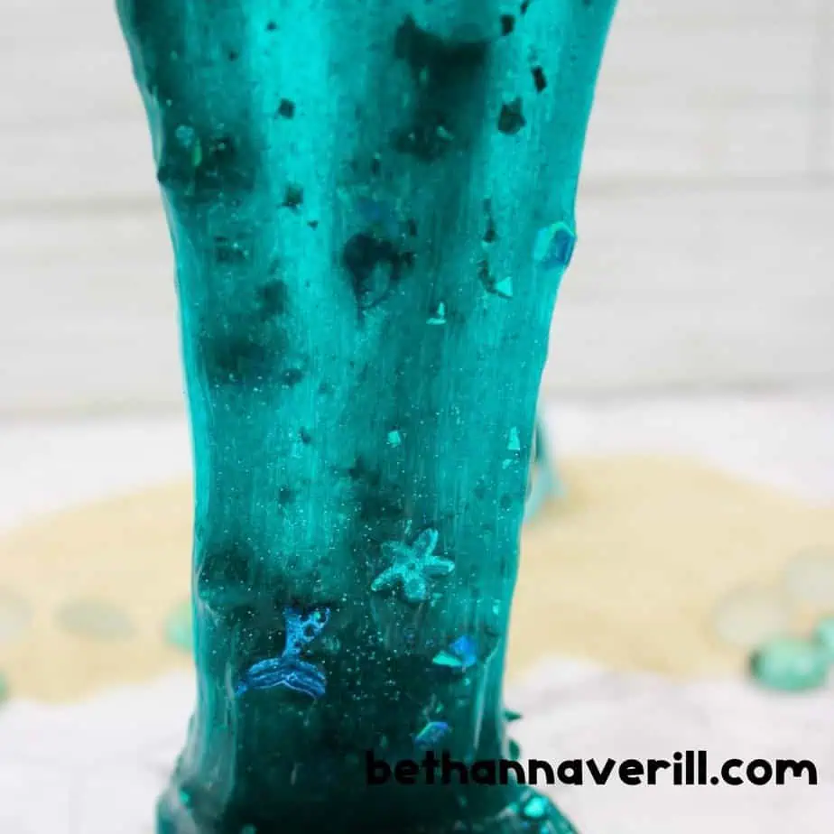 Shimmery teal mermaid slime with glitter and star confetti being stretched over a white surface