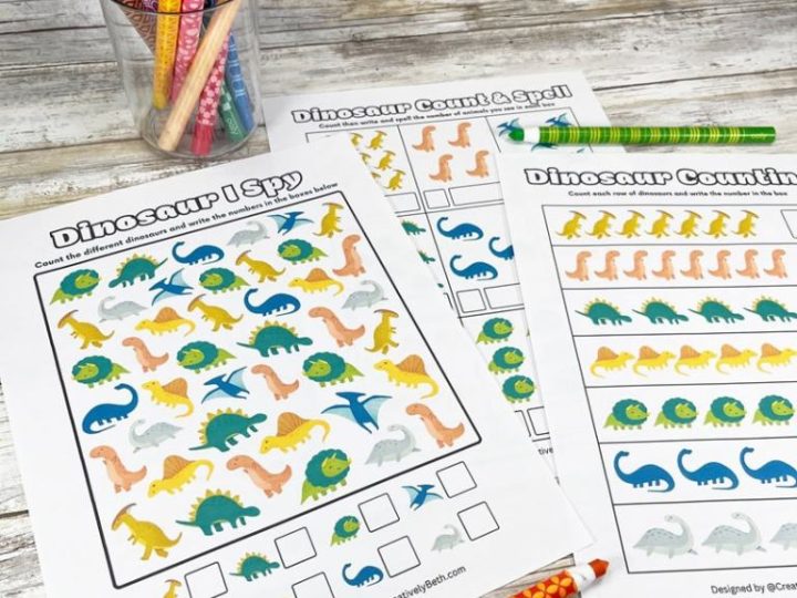 Colorful printable dinosaur counting and I Spy activity sheets spread out on a wooden surface with pencils
