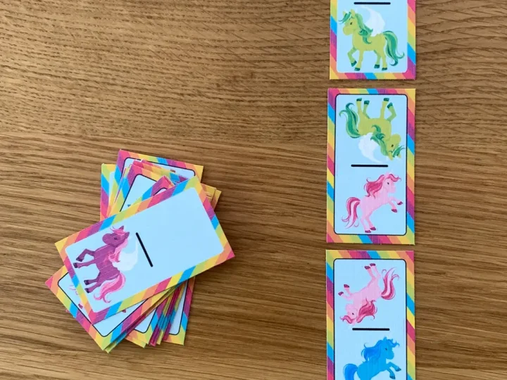 Printable rainbow unicorn dominoes spread out on a wooden table are a fun game for unicorn party crafts and activities