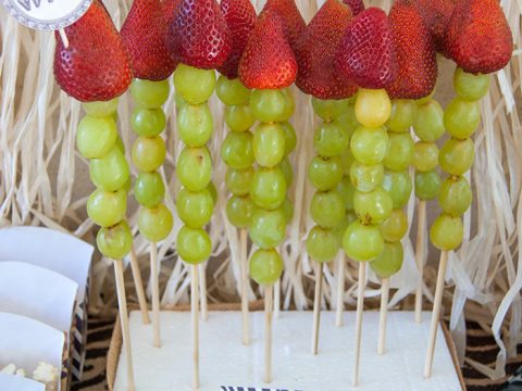 Fruit skewers with grapes and strawberries displayed on a burlap stand with safari party printables, festive safari animal party food ideas