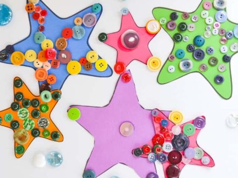 Five colorful foam starfish crafts decorated with assorted buttons and glass gems on a white surface