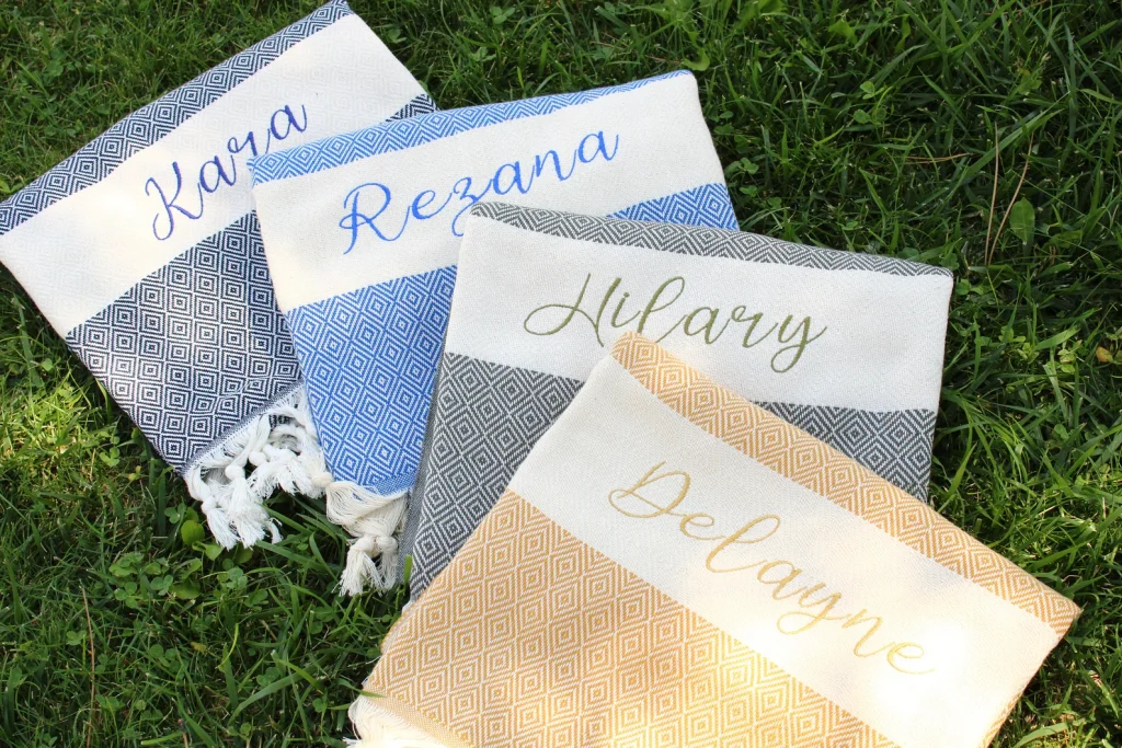 Monogrammed Turkish beach towels with diamond weave patterns in blue, gray, and gold, elegant personalized pool party favors with tassels.