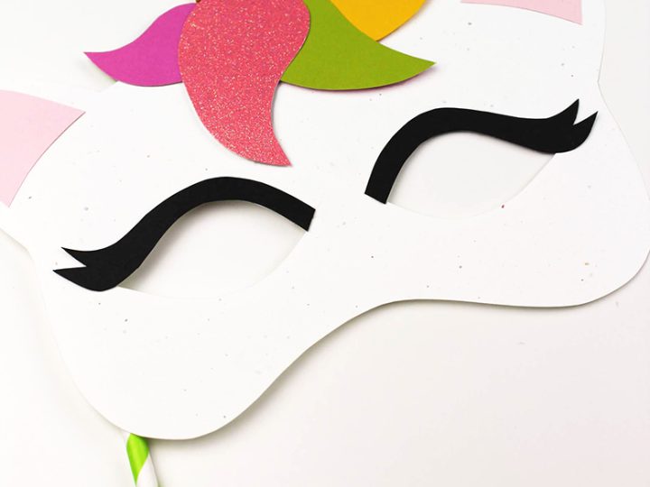 A foam sheet unicorn mask with a glitter horn colorful mane pieces and long lashes on a paper straw is a fun unicorn party craft and activity
