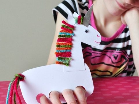 A girl holds a white paper unicorn hand puppet with colorful yarn mane perfect for unicorn party crafts and activities