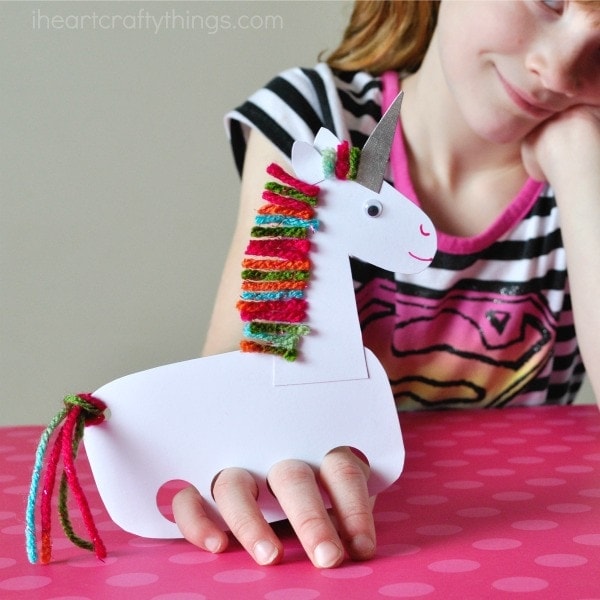 A girl holds a white paper unicorn hand puppet with colorful yarn mane perfect for unicorn party crafts and activities