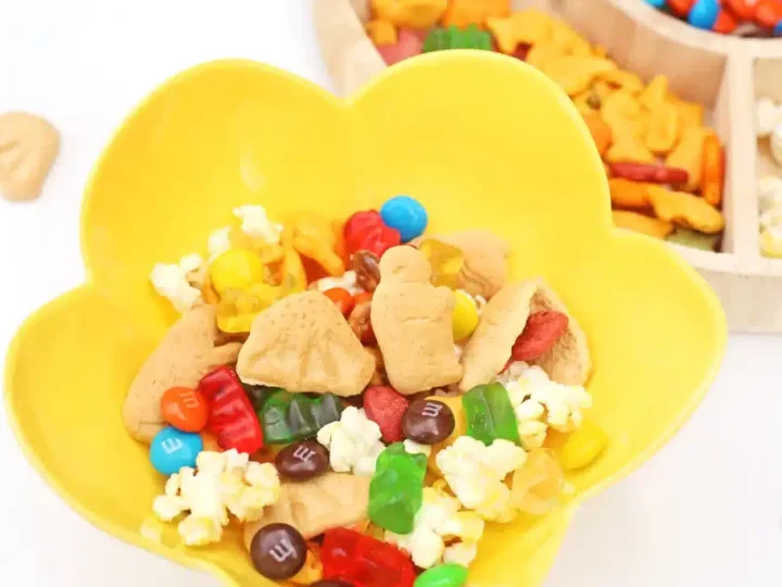 Colorful zoo snack mix with animal crackers, M&Ms, gummy bears, and popcorn in a yellow bowl, an easy safari animal party food idea