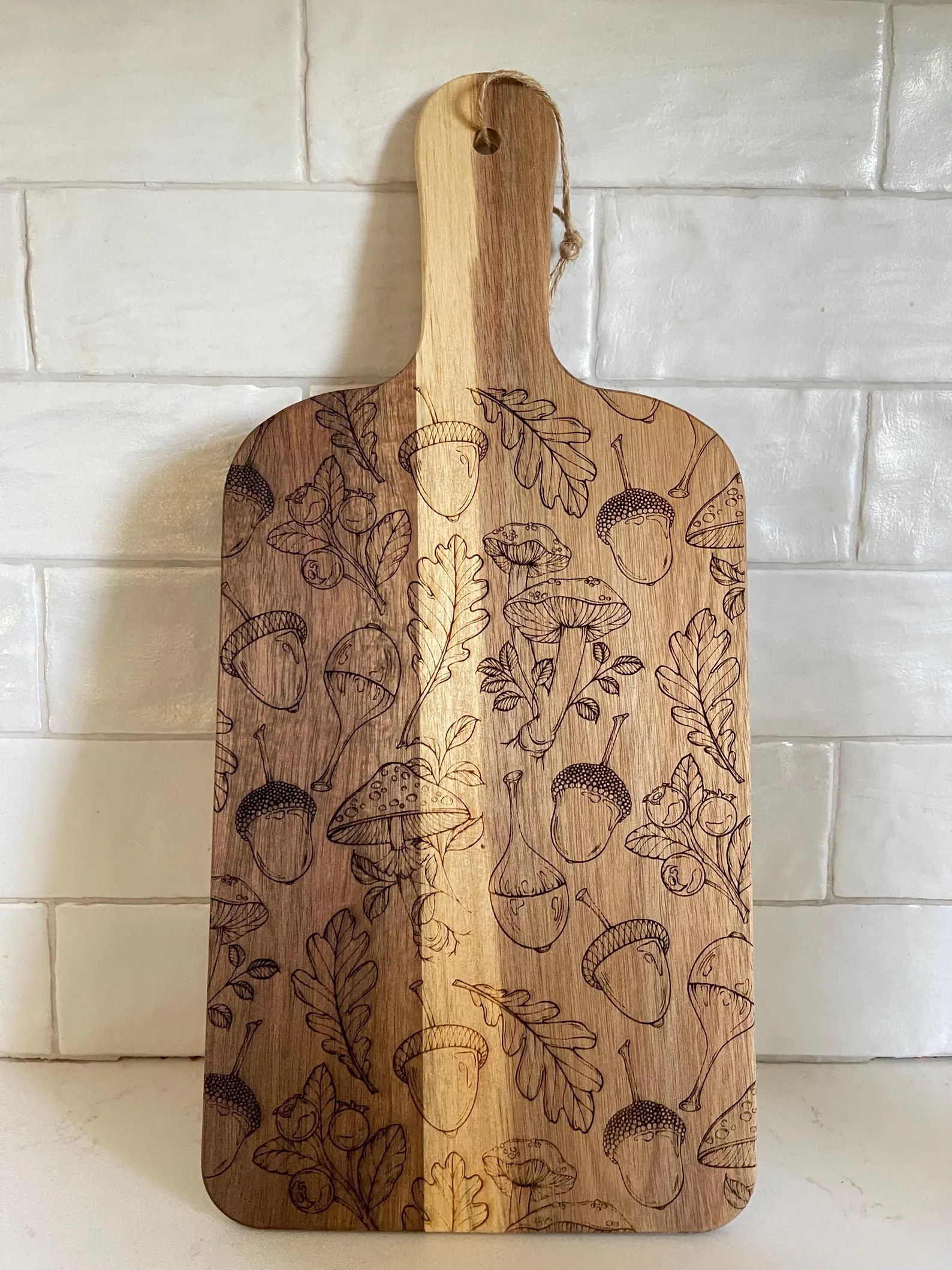 Engraved wooden serving board with acorns, mushrooms, and oak leaves design — a beautiful and unique Thanksgiving hostess gift idea for fall.