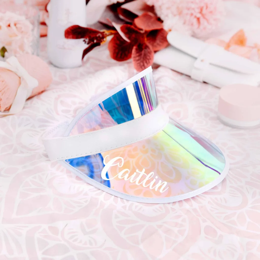 Personalized holographic iridescent sun visor with custom name in script lettering surrounded by flowers, trendy pool party favors.
