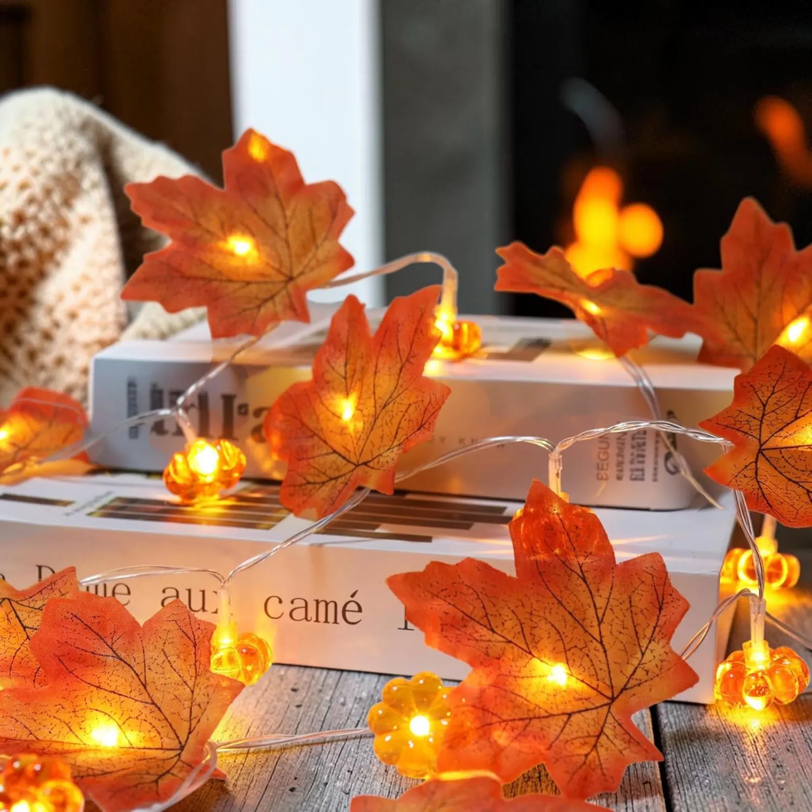 Alt text: "Warm-glowing string lights with orange maple leaves and mini pumpkins draped over books — a charming Thanksgiving hostess gift idea for fall decorating.