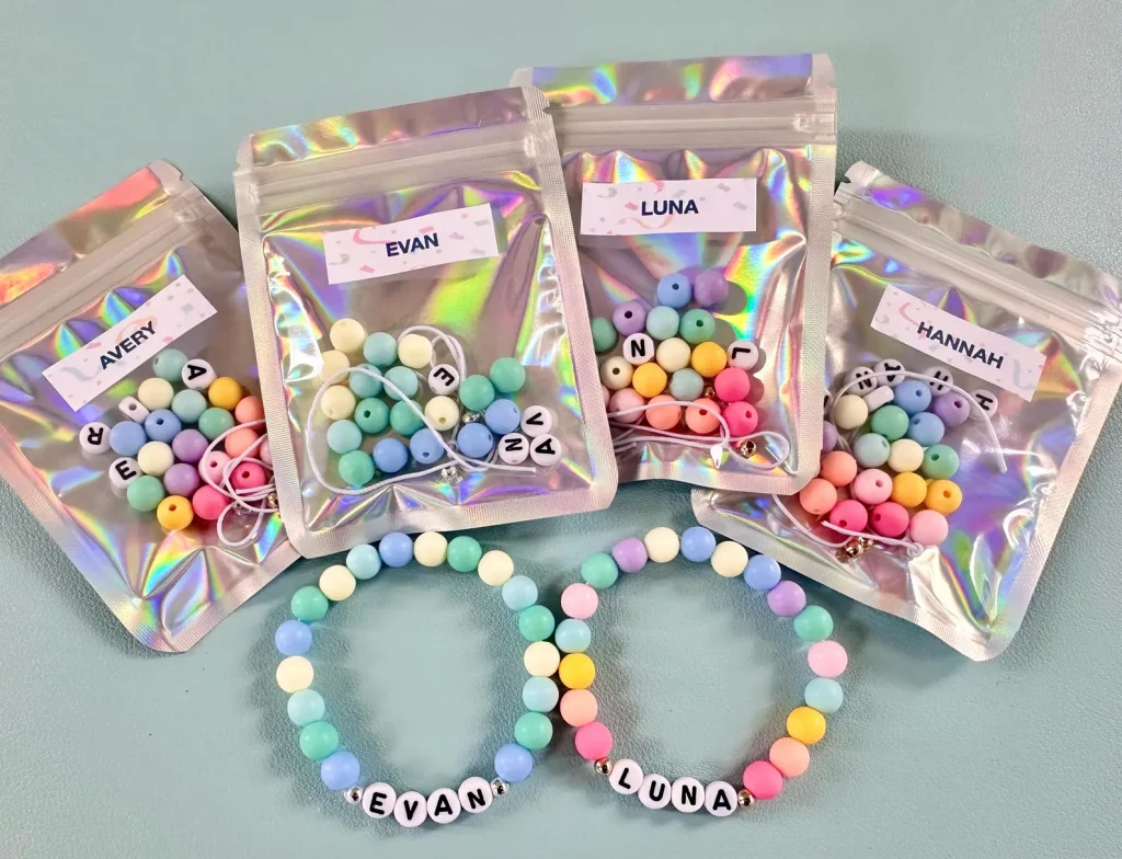 Holographic personalized DIY friendship bracelet kits with pastel silicone beads and letter beads, displayed alongside completed name bracelets — delightful tween girl party favors.