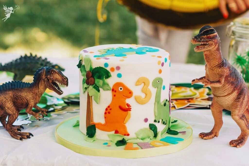 colorful dinosaur fondant birthday cake with plastic dinosaurs for birthday party table