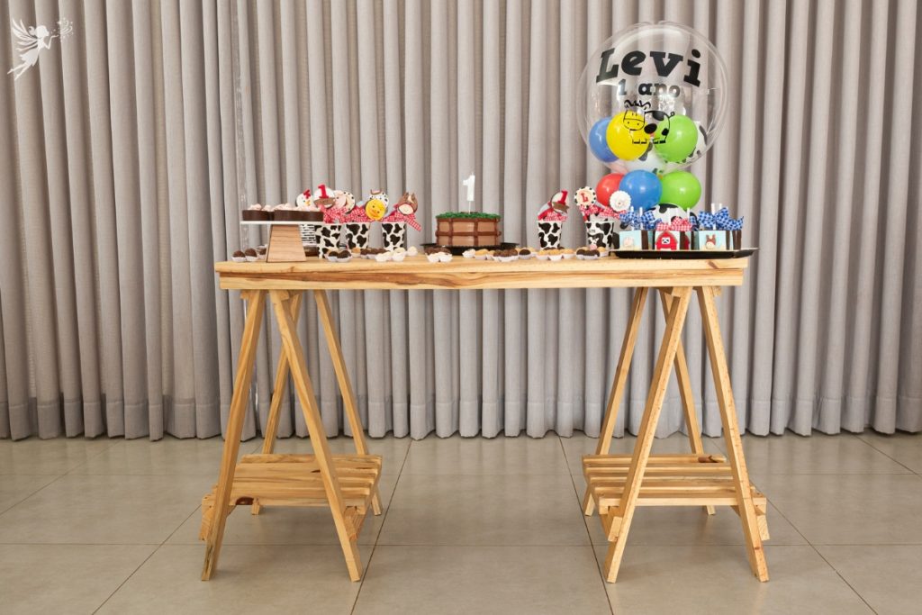 table set u for a first birthday party with decorated cow cups containing barn animal cake pops and a big balloon