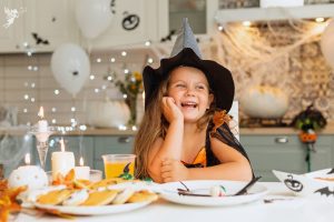 girl in witches hat smiling laughing at table with fall and halloween decorations