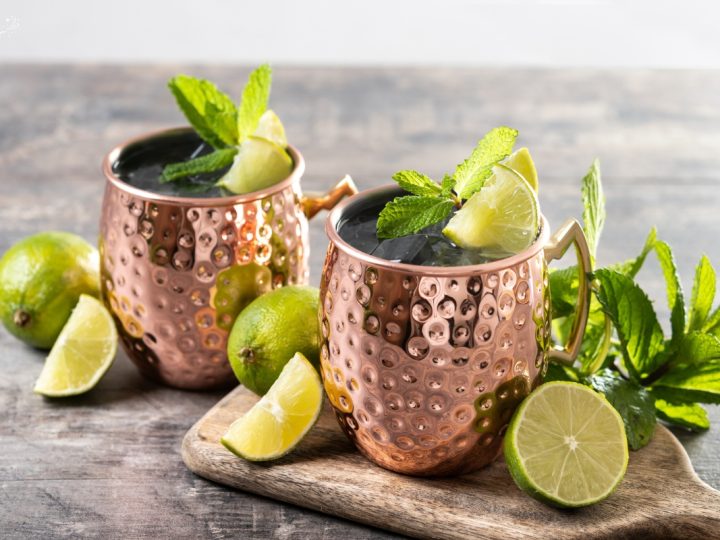 close up of two moscoe mule copper mugs sitting on an aesthetic kitchen bench setting with line and mint leaves