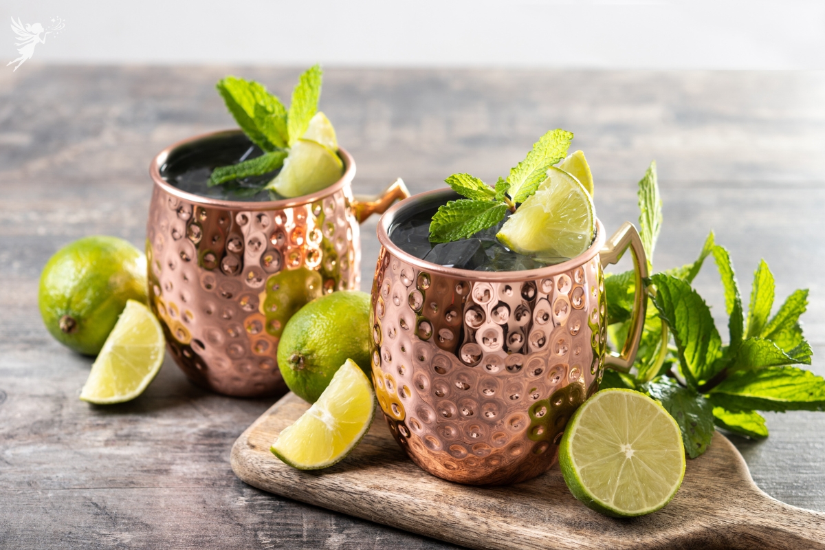 close up of two moscoe mule copper mugs sitting on an aesthetic kitchen bench setting with line and mint leaves