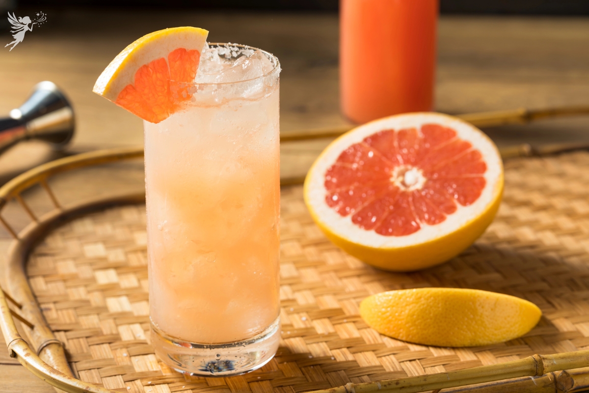 grapefruit paloma drink sitting on a ratten serving tray with a grapefruit slice and a grapefruit cut open