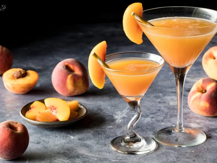 close up of two glasses of beach belini dark endch top background with peach slices scattered