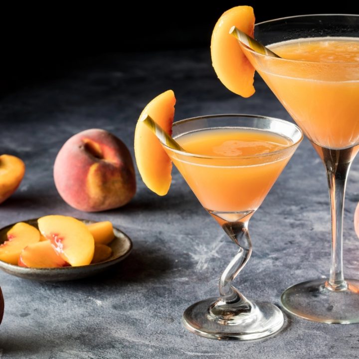 close up of two glasses of beach belini dark endch top background with peach slices scattered