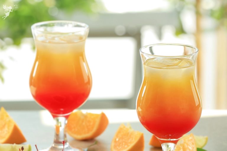 close up of two orange sunrise mocktail drinks on a kitchen counter with orange slices