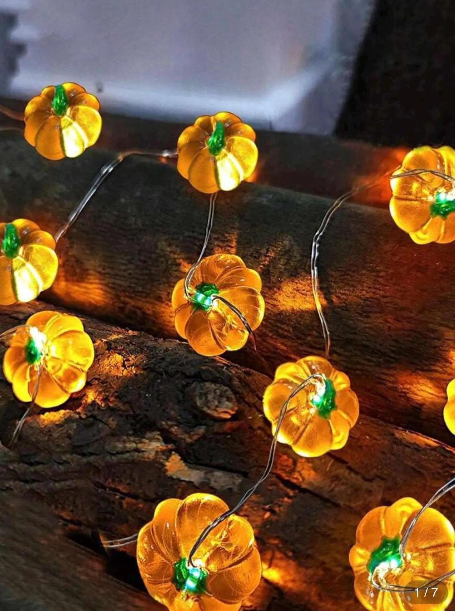 Glowing LED pumpkin string lights draped over rustic wood logs, a cozy and festive choice among Thanksgiving hostess gift ideas for fall decor.