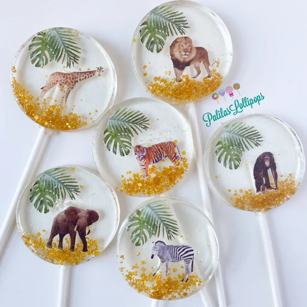 Safari animals party favor ideas featuring clear round lollipops embedded with realistic giraffe, lion, tiger, elephant, zebra, and gorilla images with gold sugar crystals.
