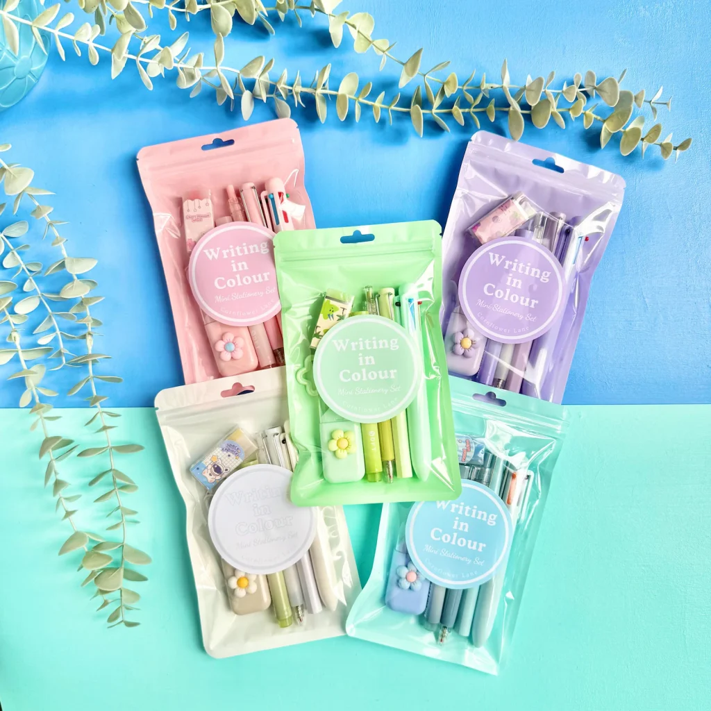 Five pastel "Writing in Colour" mini stationery sets in pink, green, purple, white, and blue pouches with pens, erasers, and flower clips — practical tween girl party favors.