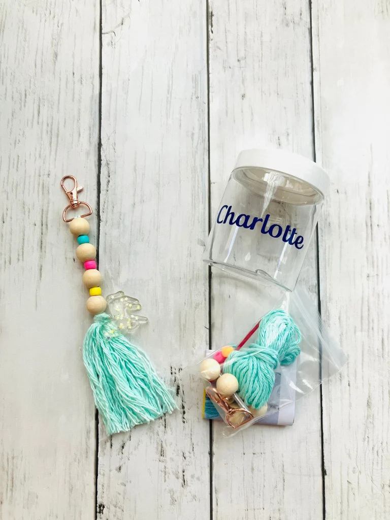 Personalized DIY backpack charm kit in a labeled clear jar featuring colorful wooden beads, mint tassel, and rose gold clip — creative tween girl party favors.