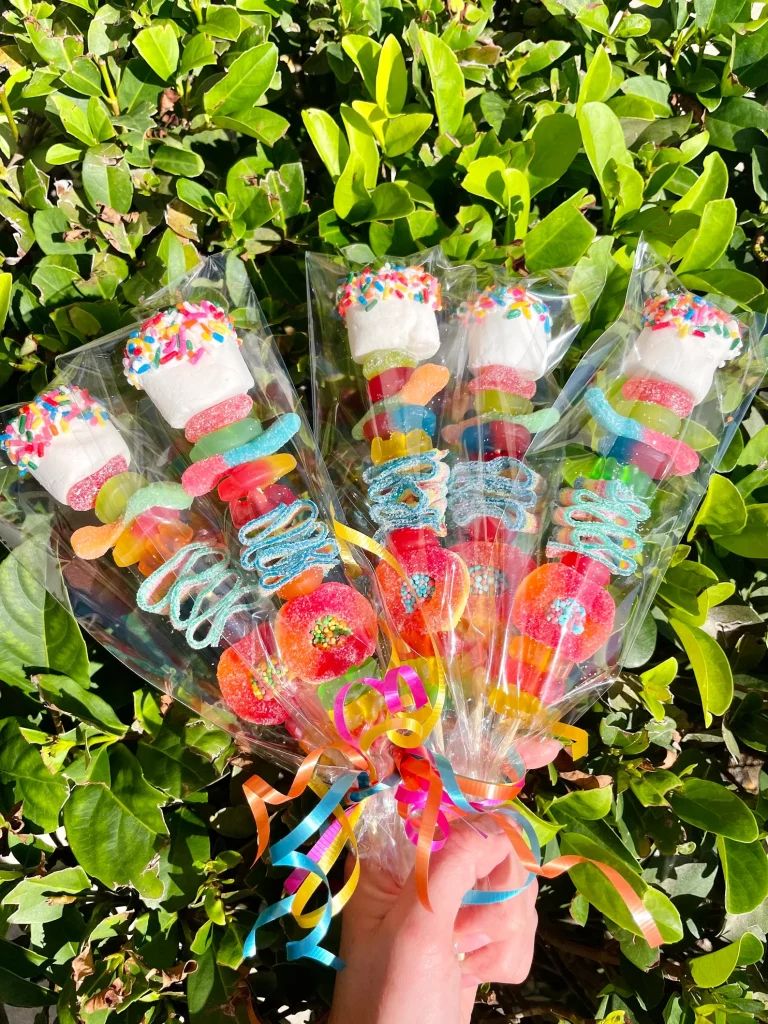 Colorful candy kabobs loaded with gummy candies, sprinkle-dipped marshmallows, and sour worms wrapped in clear bags with ribbon — irresistible tween girl party favors.