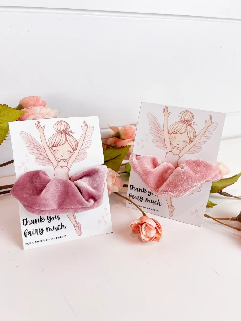 Dusty pink velvet scrunchies mounted on illustrated fairy ballerina thank you cards surrounded by pink florals make sweet and stylish fairy party favors for a girls birthday party
