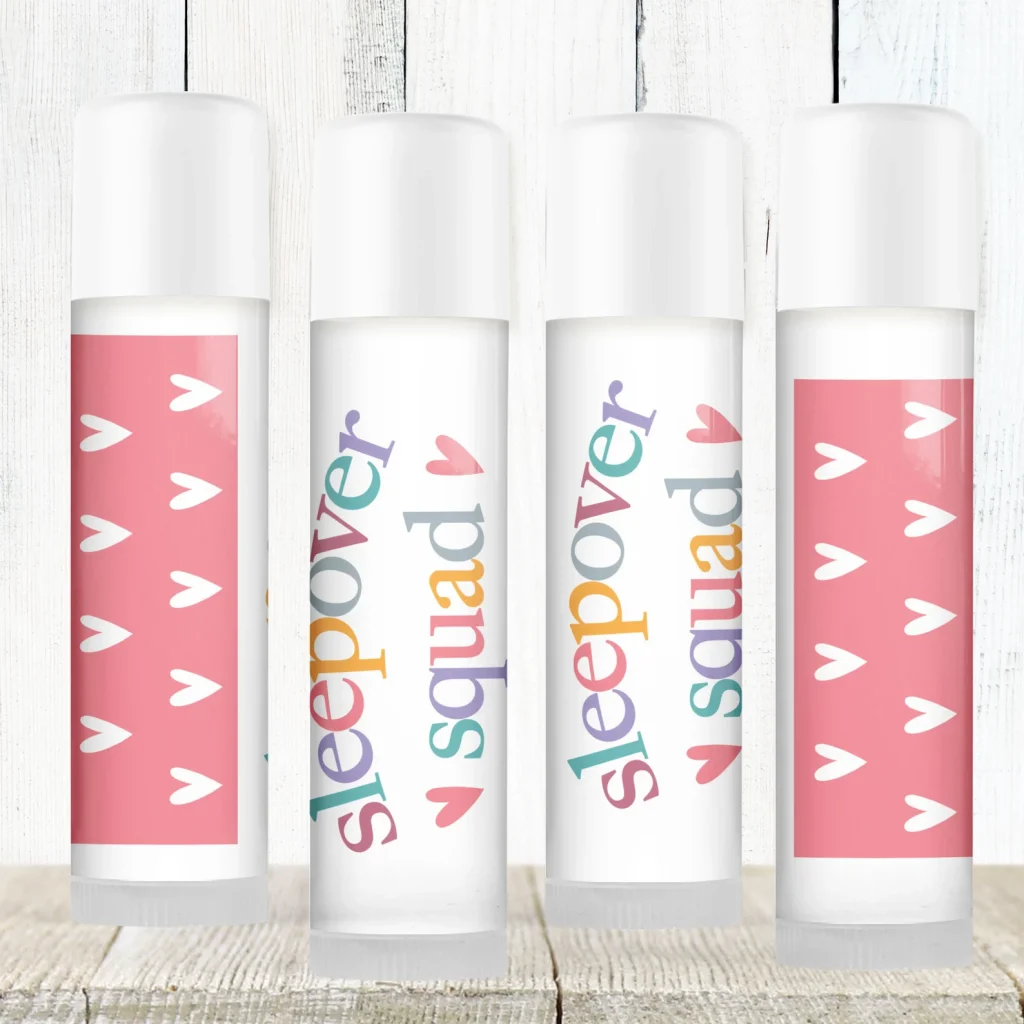 Four customized lip balm tubes with colorful "Sleepover Squad" labels and pink heart designs, making sweet and practical tween girl party favors.