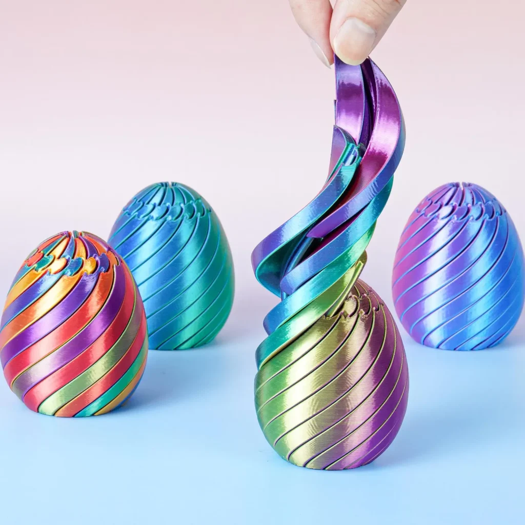 Four metallic rainbow swirl fidget eggs in red, blue, green, and purple that stretch and spiral open, making uniquely satisfying tween girl party favors.