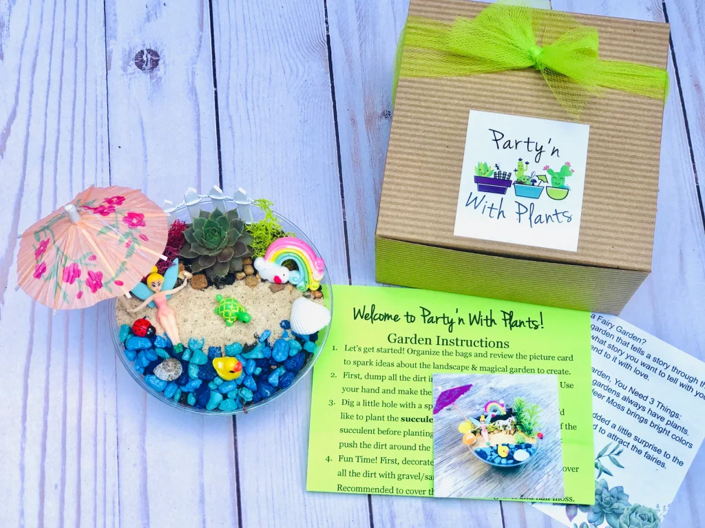 A mini fairy garden kit in a glass bowl filled with blue pebbles sand a succulent tiny fairy figurine and colorful miniature accessories packaged in a kraft box with green ribbon makes a magical fairy party favor for a birthday party