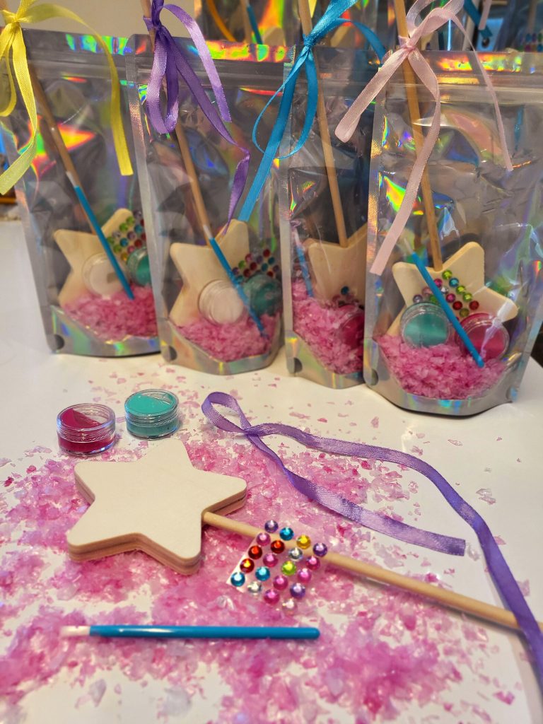 Paint your own wooden star wand kits with glitter paint pots colorful rhinestone stickers and satin ribbons packed in holographic bags make an enchanting hands on activity as fairy party favors for a girls birthday party