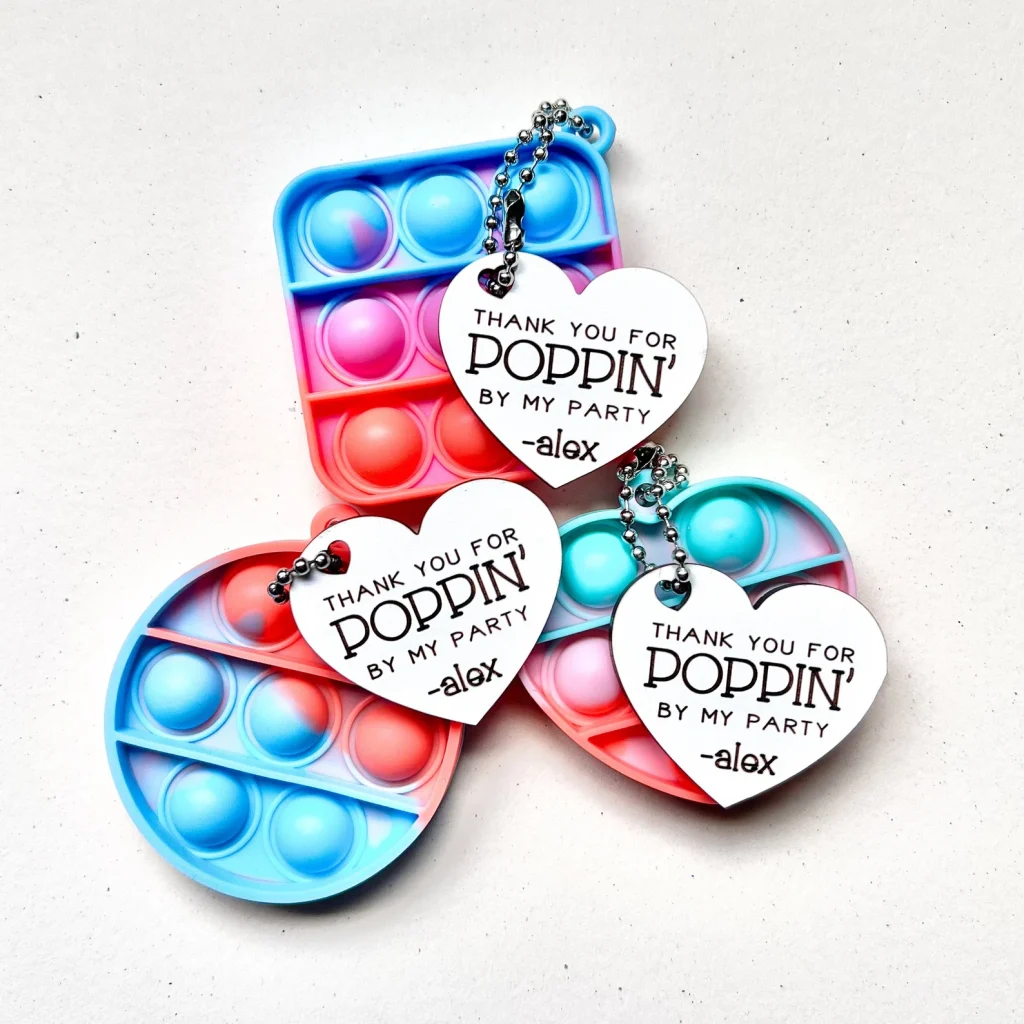 Tie-dye mini pop-it keychains with personalized heart tags reading "Thank You for Poppin' By My Party" — fun and colorful tween girl party favors.