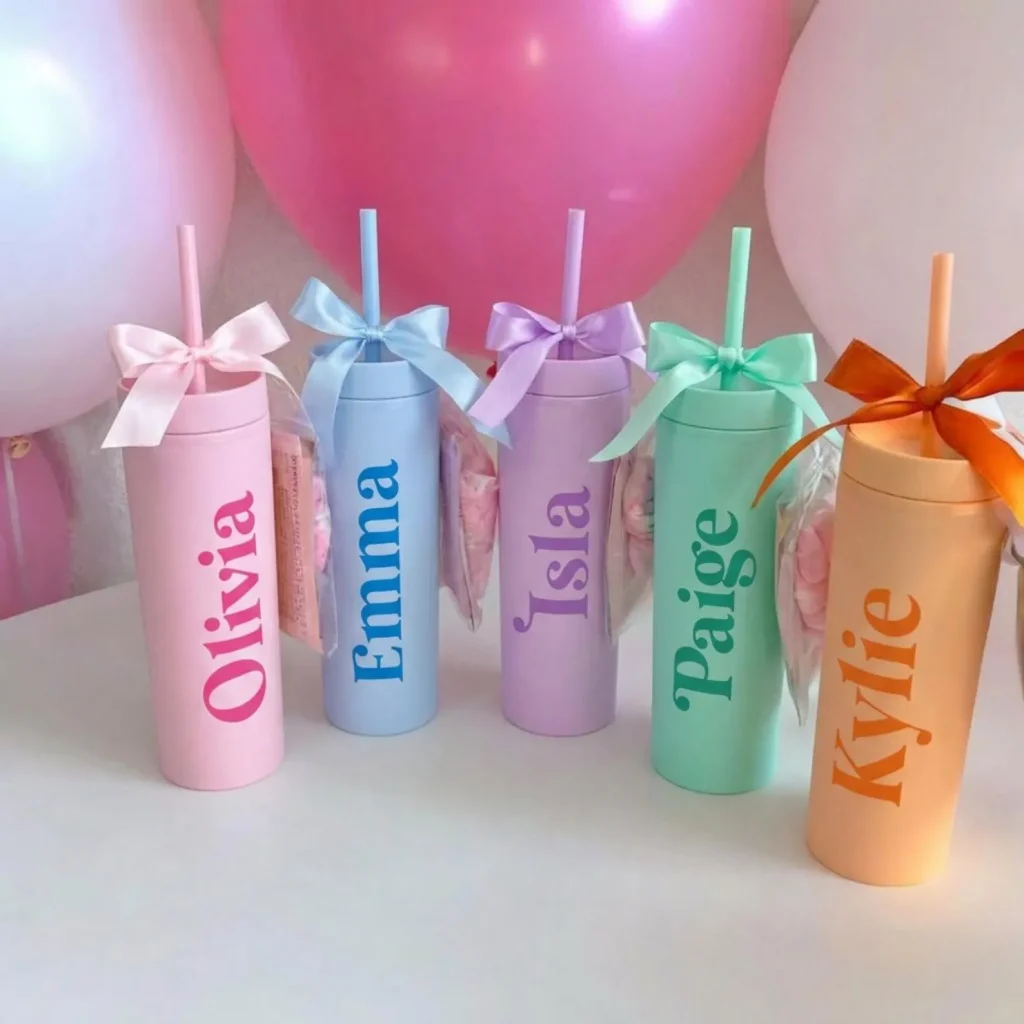 Five pastel personalized skinny tumblers in pink, blue, purple, mint, and orange with matching ribbon bows and straws — trendy tween girl party favors.