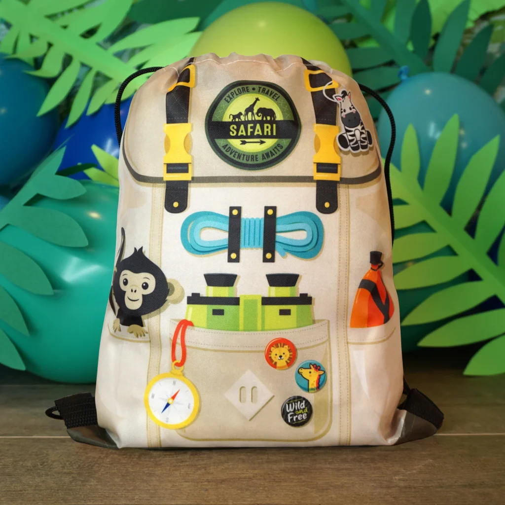 Safari animals party favor ideas including a tan drawstring backpack printed with safari adventure imagery, compass, binoculars, monkey, zebra, and "Wild and Free" badge.