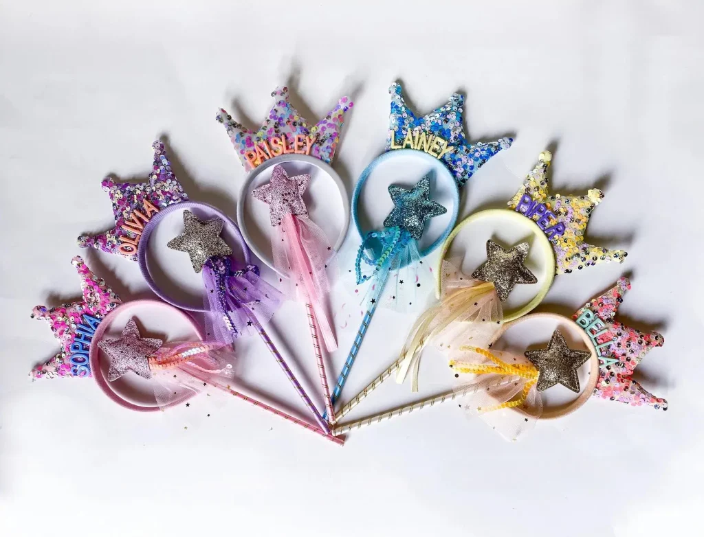 Personalized sequin crown headbands paired with matching glitter star wands and flowing tulle streamers in pastel pink purple blue and yellow make sparkly fairy party favors for a girls birthday celebration