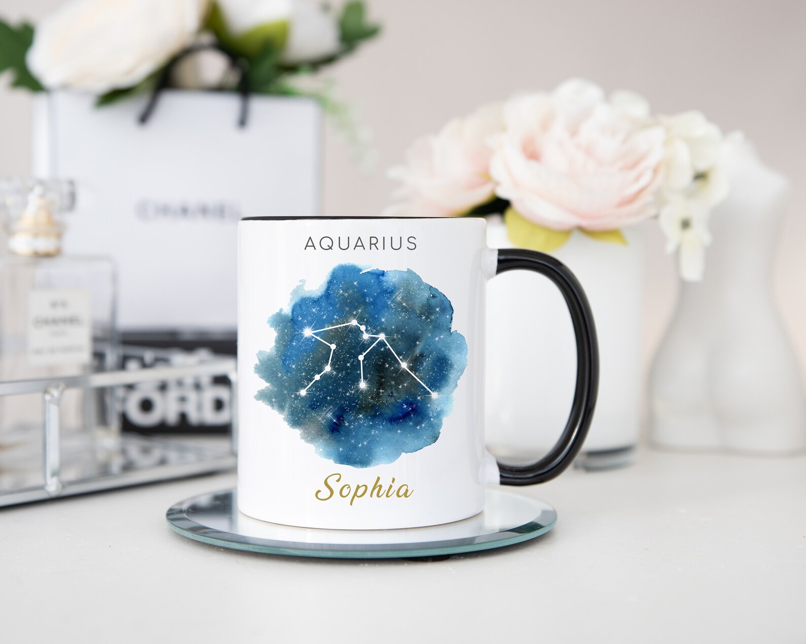 A white and black ceramic mug printed with a watercolor galaxy Aquarius constellation and a personalized gold name, a chic February birthday gift idea.