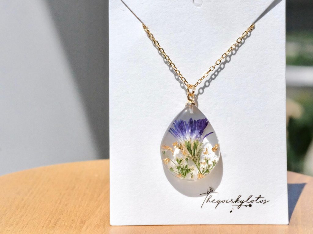 Teardrop resin pendant necklace with a pressed purple aster flower and gold flakes, a delicate choice for September birthday gift ideas.