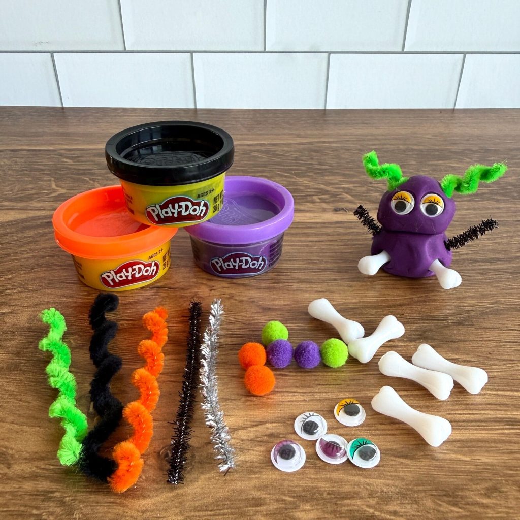 Make-your-own Play-Doh monster kit with pipe cleaners, googly eyes, pom-poms, and bone pieces, a creative Halloween party favor for kids.