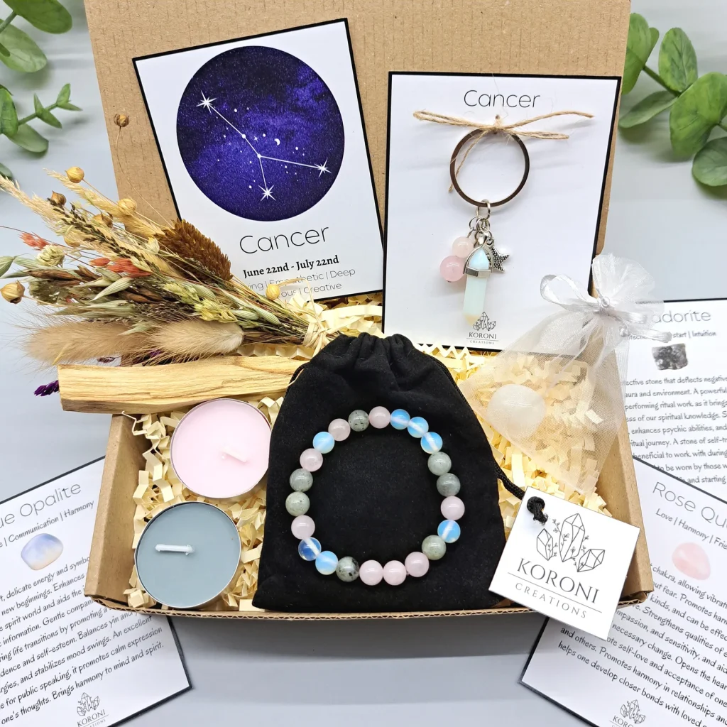 Cancer zodiac crystal gift box containing a beaded gemstone bracelet, constellation keychain, rose quartz heart, candles and dried flowers, a thoughtful July birthday gift idea.
