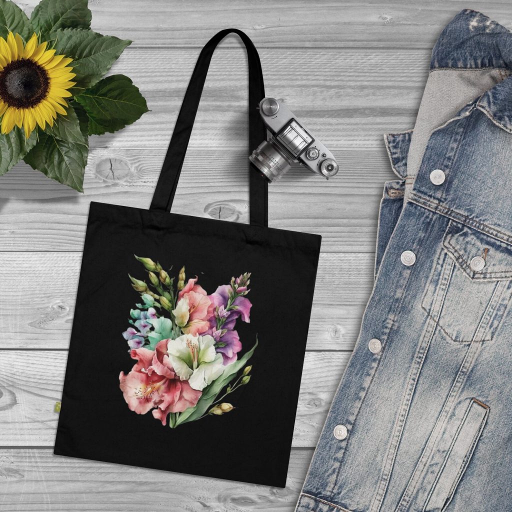A black canvas tote bag printed with a vibrant watercolor gladiolus bouquet in pink, white and purple, a stylish and everyday August birthday gift idea.
