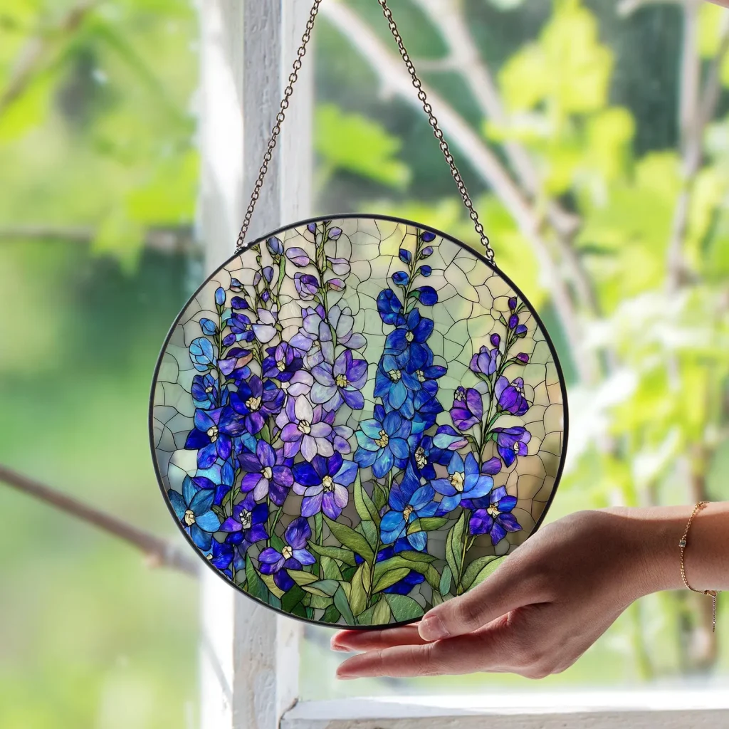 A round stained glass window suncatcher featuring purple and blue larkspur blooms on a chain, a beautiful and unique July birthday gift idea.