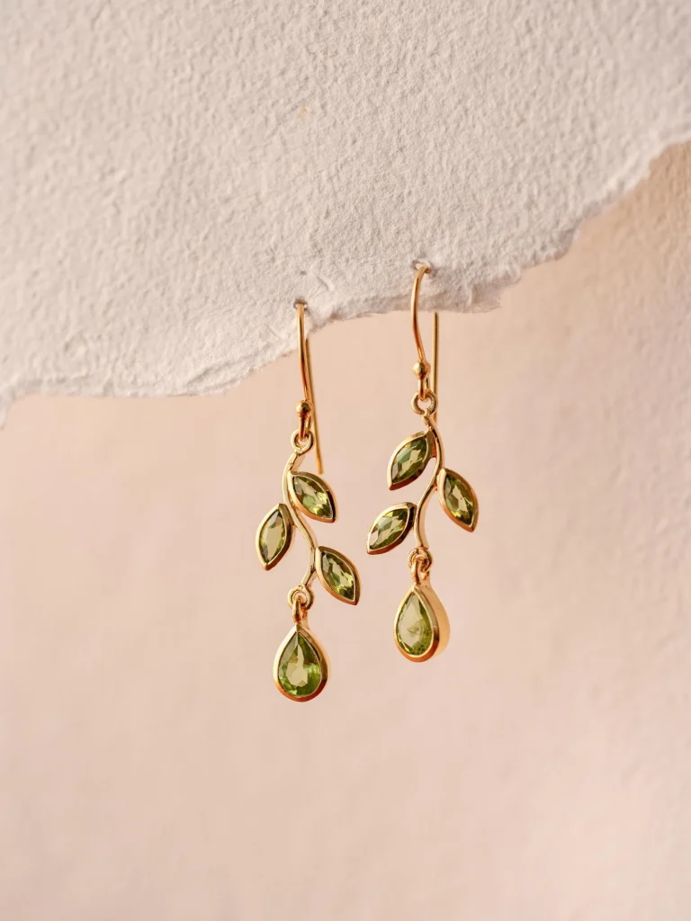 Gold wire earrings shaped like delicate leaf branches set with marquise and teardrop peridot gemstones, a nature-inspired August birthday gift idea.