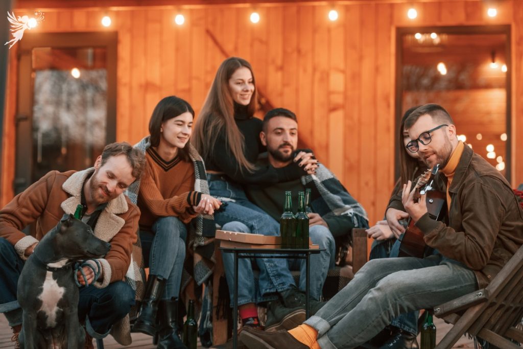 friends gathered outside a cabin with string lighting, playing guitar