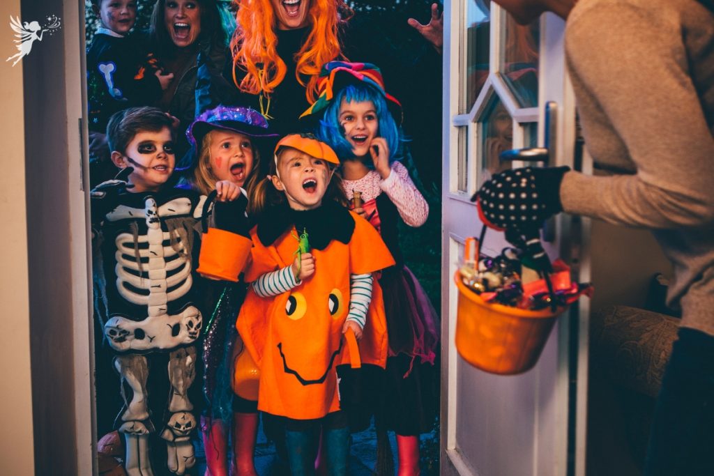 mother opening door to trick or treating children with a bucket of goodies other than candy