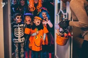 mother opening door to trick or treating children with a bucket of goodies other than candy