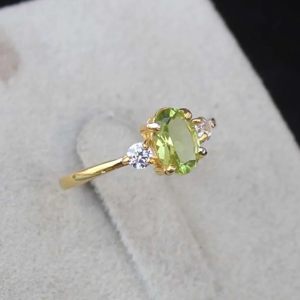 A gold ring featuring an oval peridot birthstone flanked by two round white crystals on a slim band, a classic and timeless August birthday gift idea.