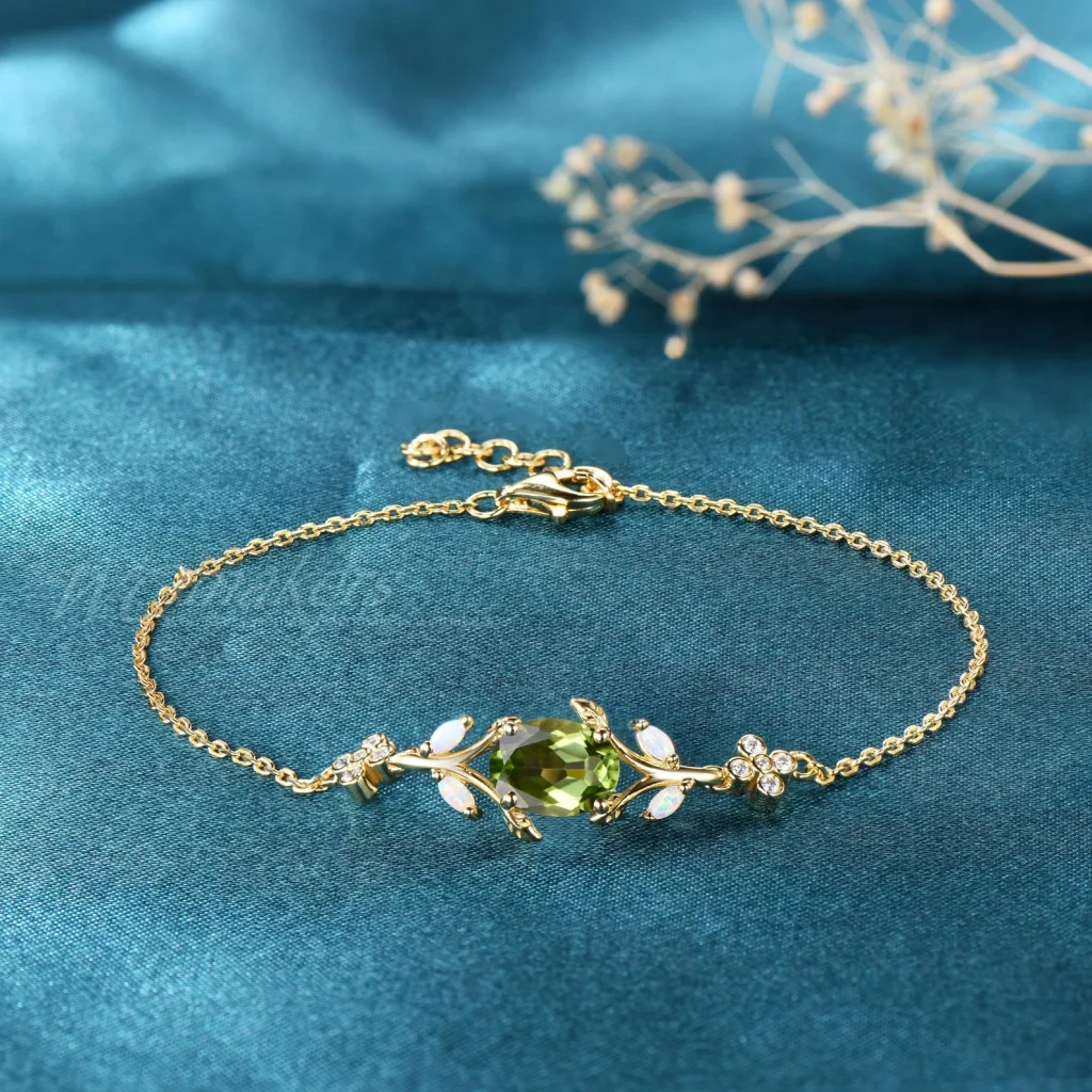 A dainty gold chain bracelet centered with an oval peridot stone flanked by opal leaf accents and crystal flowers, an elegant August birthday gift idea.
